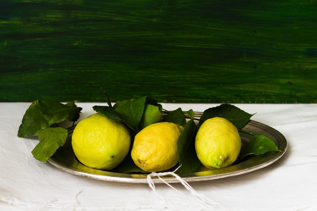Three lemons with leaves on a tray