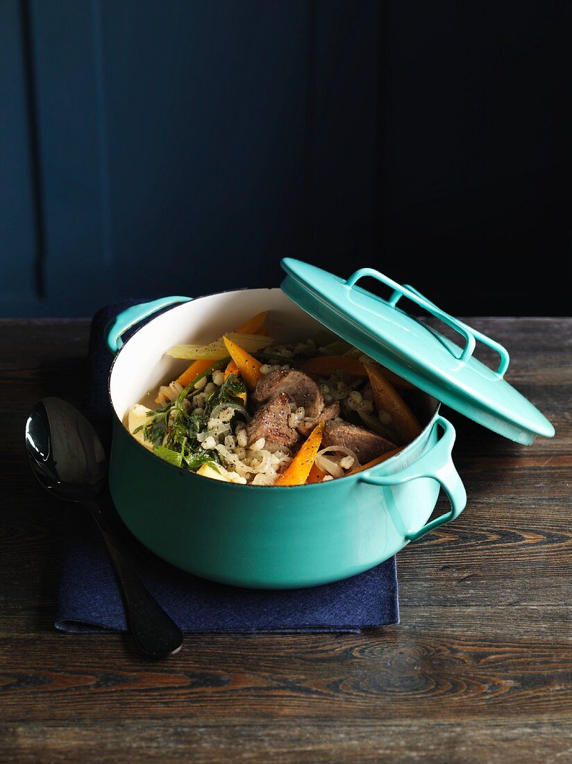 Pork stew with vegetables and tender wheat in a light blue enamel pot