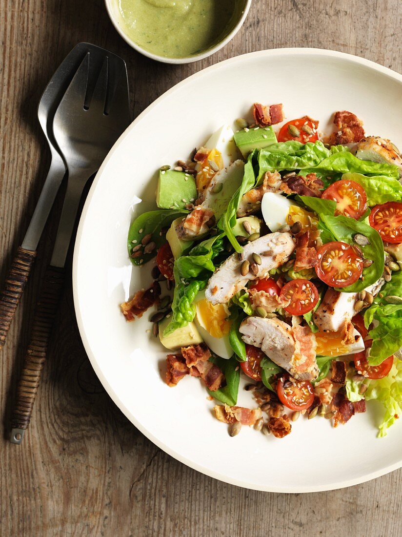 A mixed salad with avocado, egg, tomatoes, bacon and chicken breast