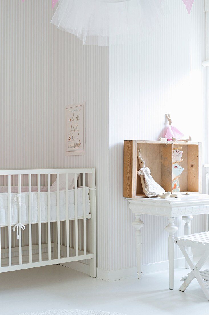 Weiß lackiertes Gitterbett und Tisch mit Hasenpuppen in Kinderzimmer mit zart gestreifter Tapete