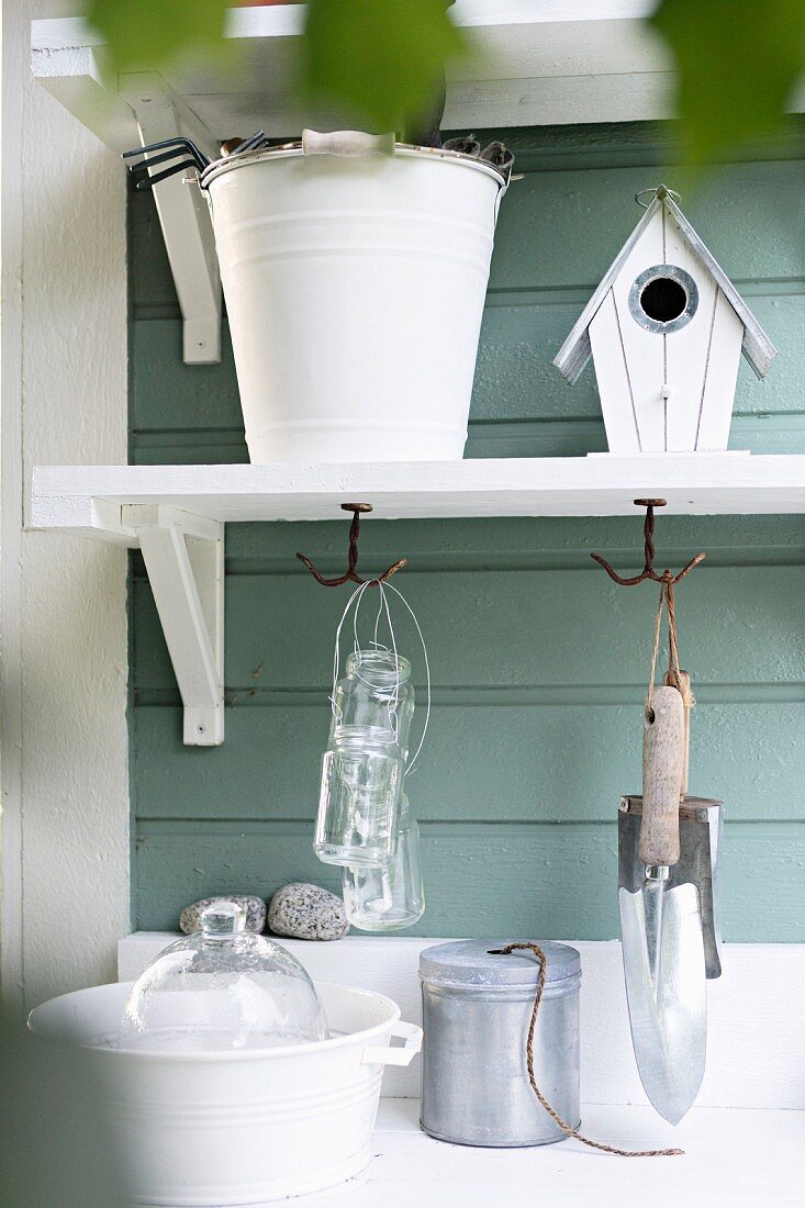 Gardening utensils on bracket shelves on green wooden wall of garden shed