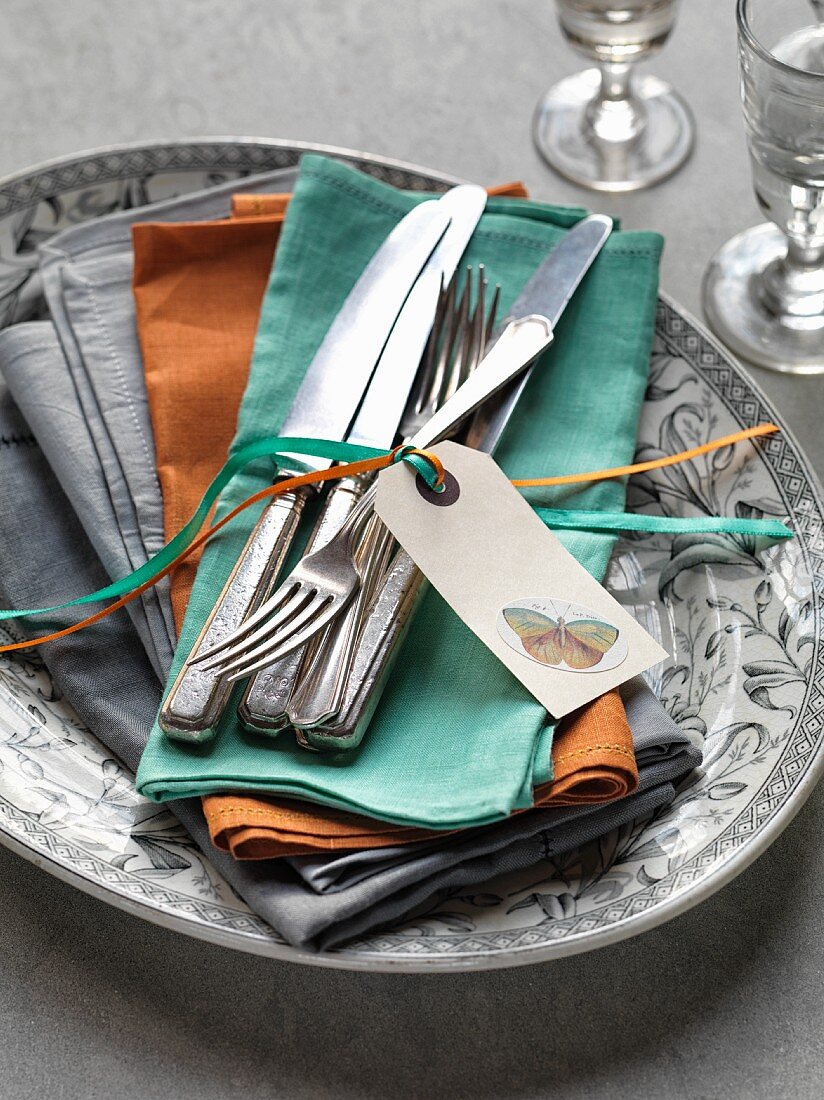 Silver cutlery with a label and ribbons on coloured napkins