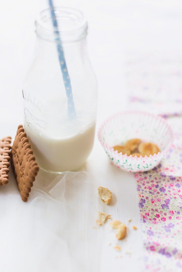 A milk bottle with a straw with butter biscuits and crumbs it