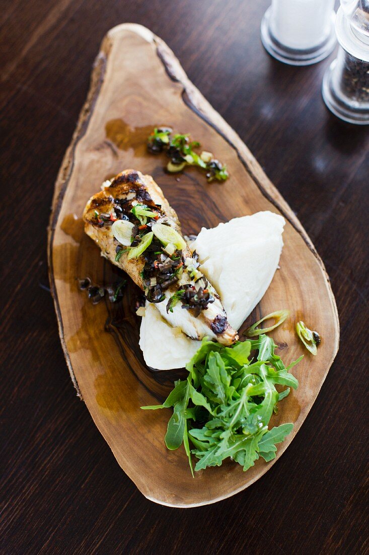 Fish with mashed potatoes and rocket on a wooden board