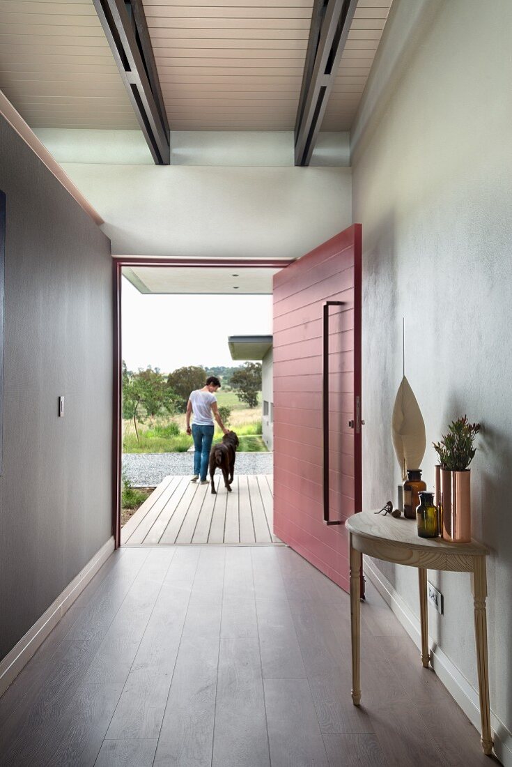 Minimalist foyer with console table, red-painted, open front door and woman and dog on porch