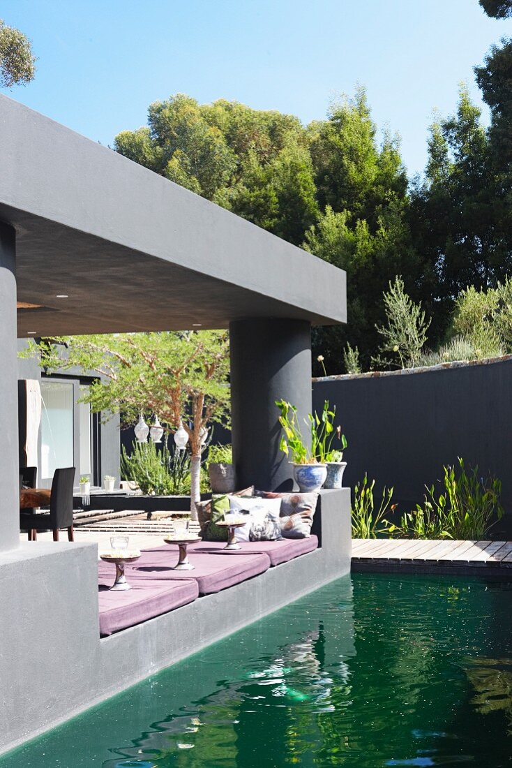 Pond outside modern house with roofed terrace painted grey and comfortable floor cushions on edge