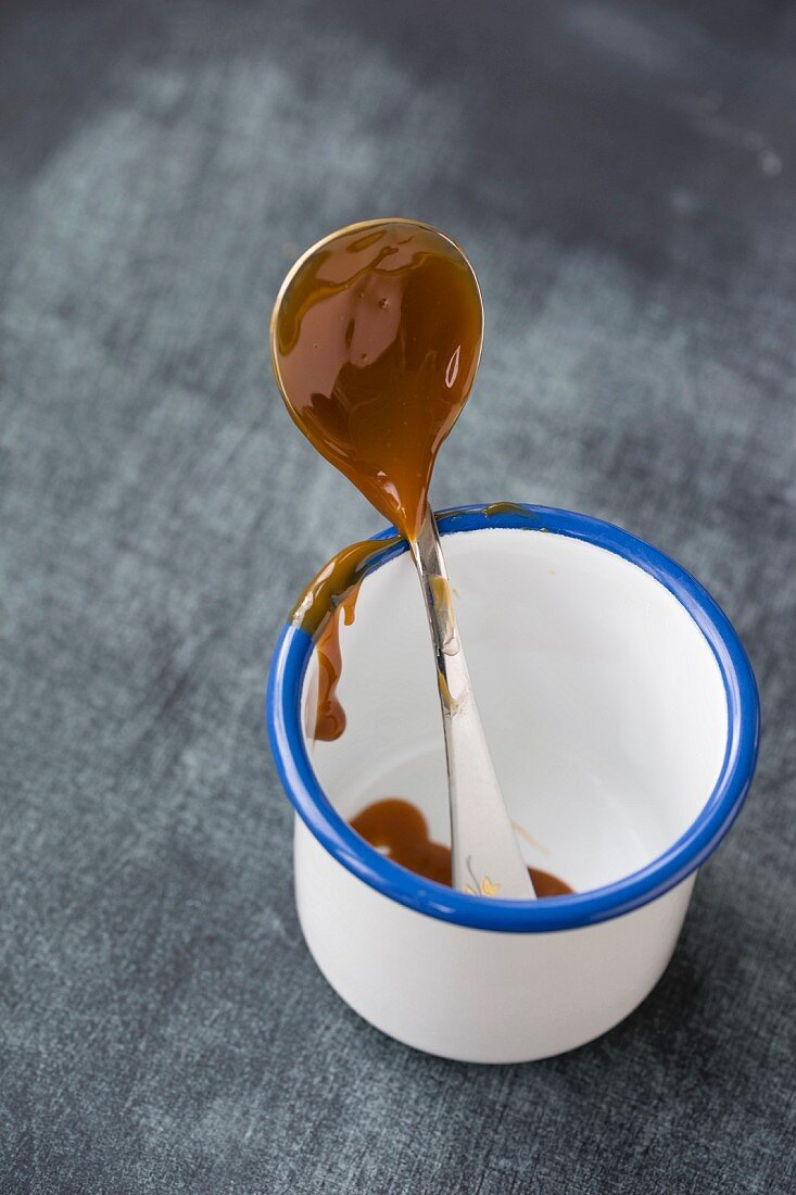 Caramel cream on a spoon in an enamel mug