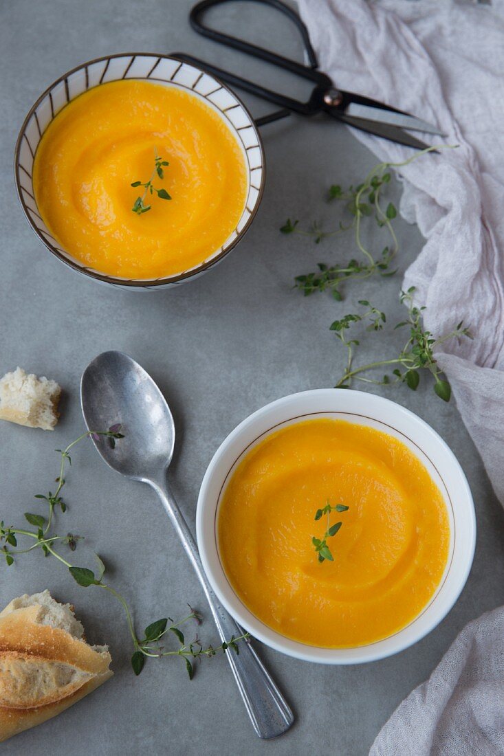 Two bowls of cream of pumpkin soup with thyme and baguette