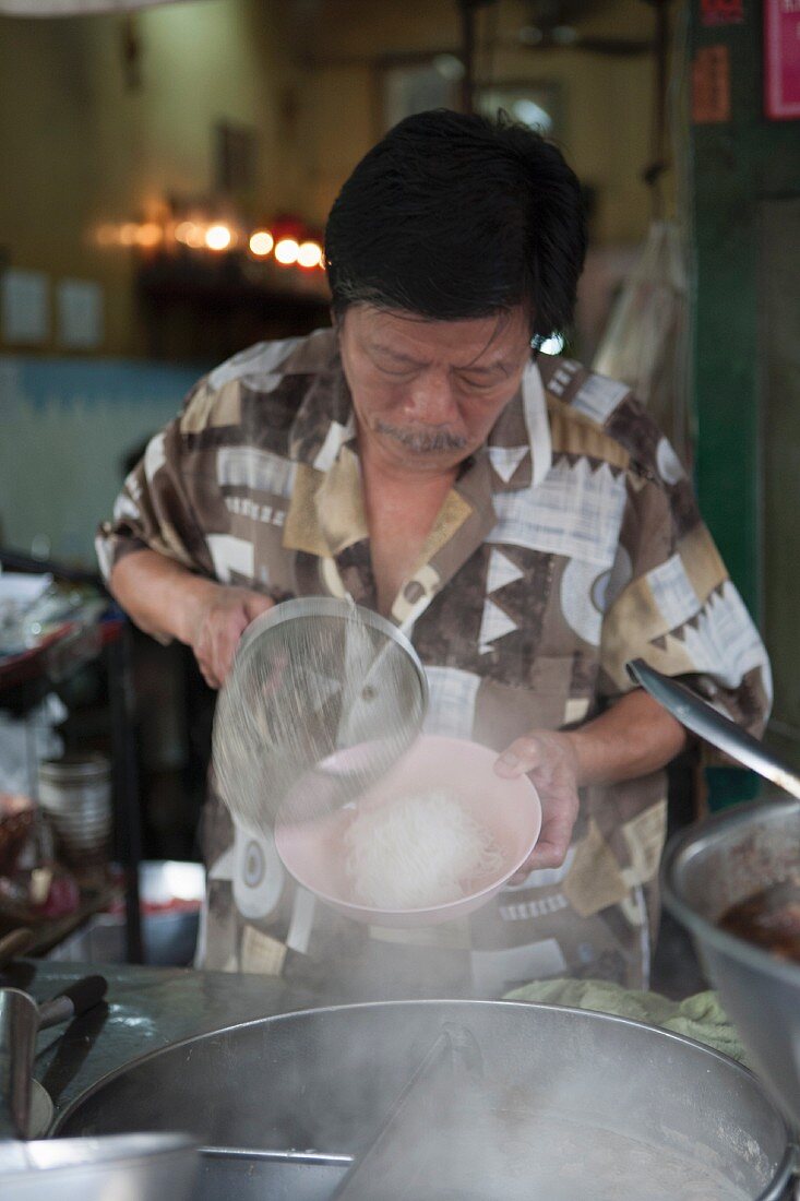 Mann kocht Nudelsuppe in einer Garküche in Thailand