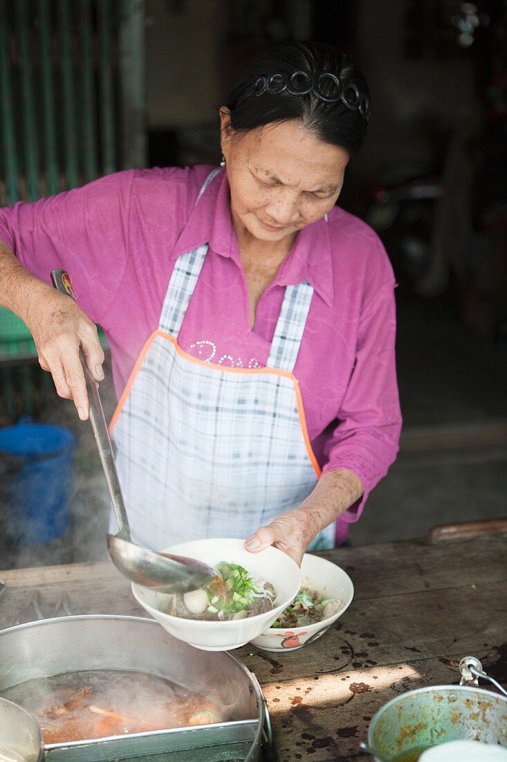 Ältere Frau beim Schöpfen von Nudelsuppe, Thailand