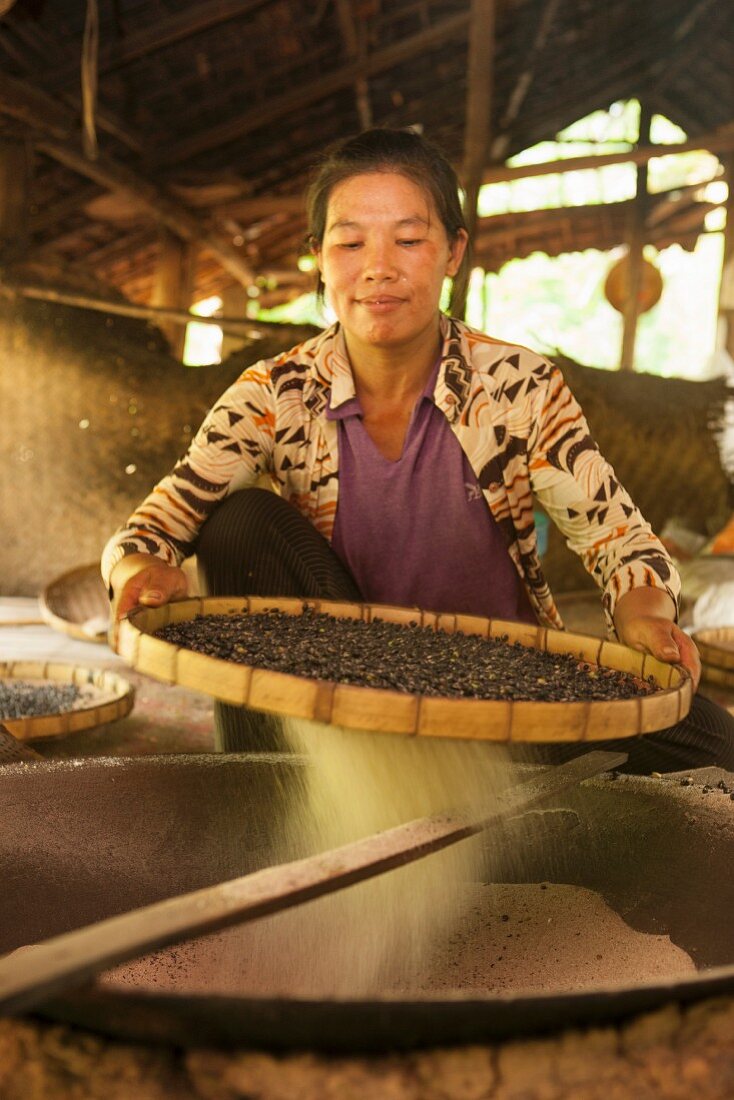 A Thai woman roasting peanuts in the traditional way