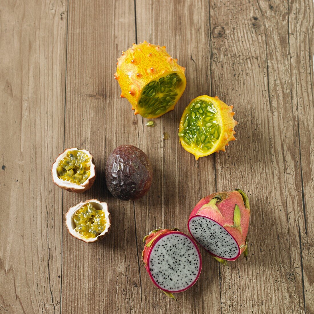 Various exotic fruits on a wooden surface over (passion fruit, red pitahaya, kiwano)