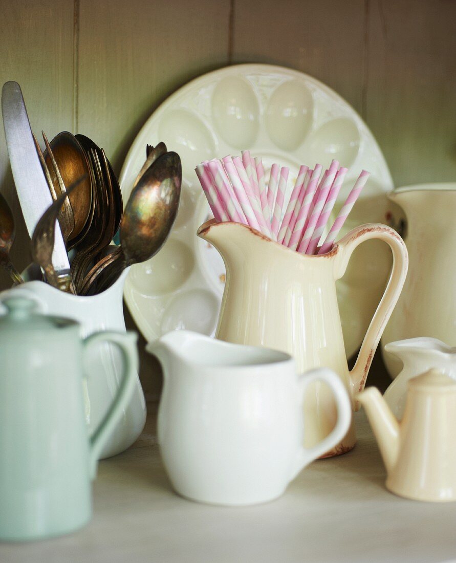 White vintage china jugs, some containing cutlery and drinking straws