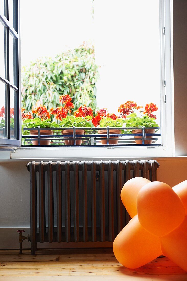 Orange 70s floor lamp below open window and potted red geraniums on windowsill
