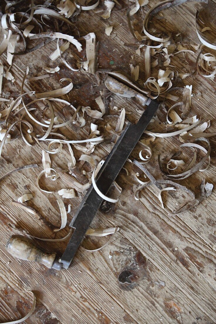 Wood shaving and traditional peeling knife on old wooden floor in carpenter's workshop