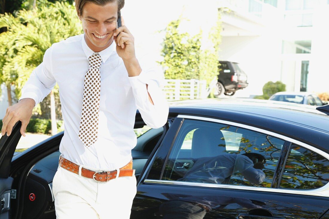 A young businessman holding a tablet computer standing next to a car