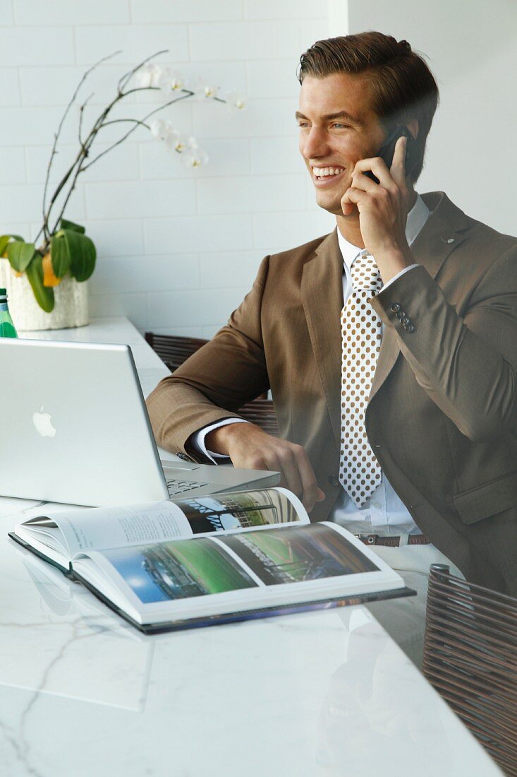 A young businessmen on the phone wearing a brown blazer sitting in an office
