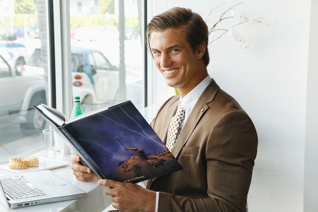 A young businessman wearing a brown blazer sitting in an office with a book