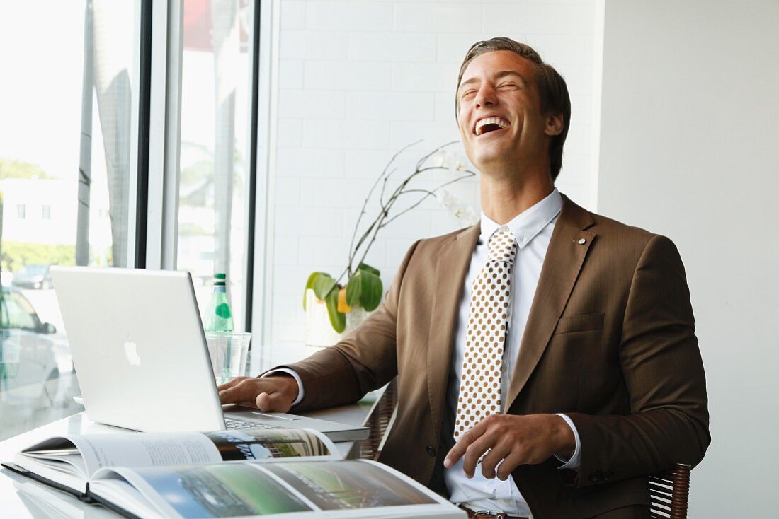 A young businessman wearing a brown blazer laughing in an office