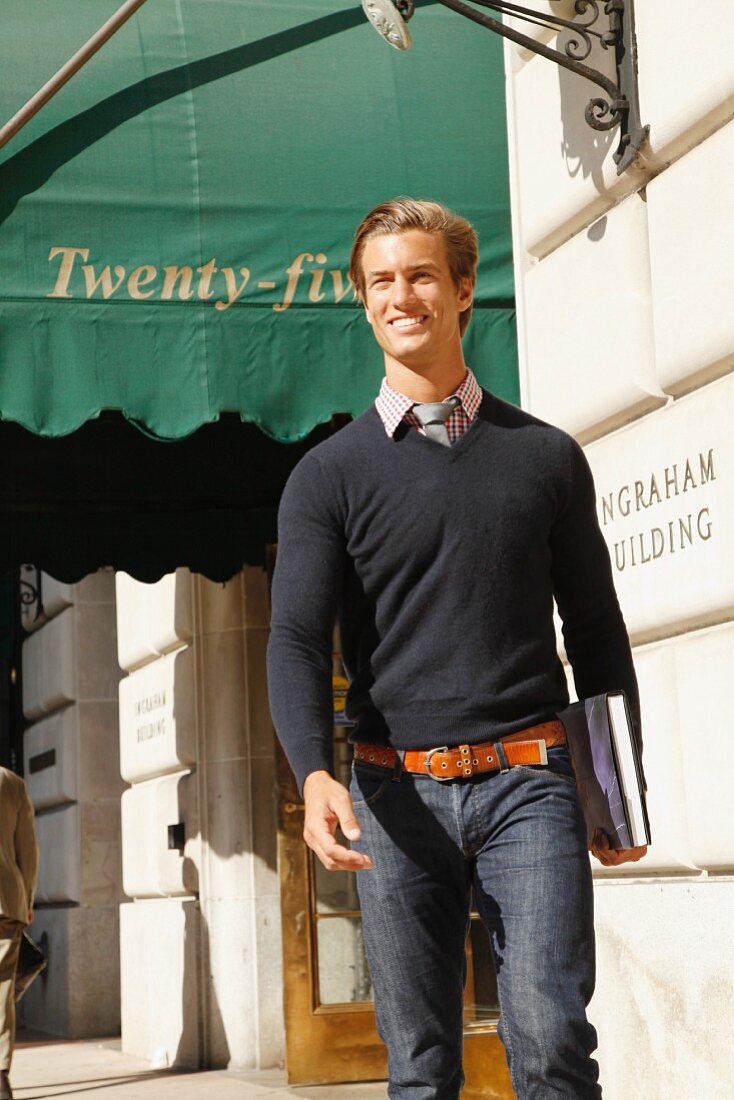 A young man wearing a jumper walking down the street holding the book