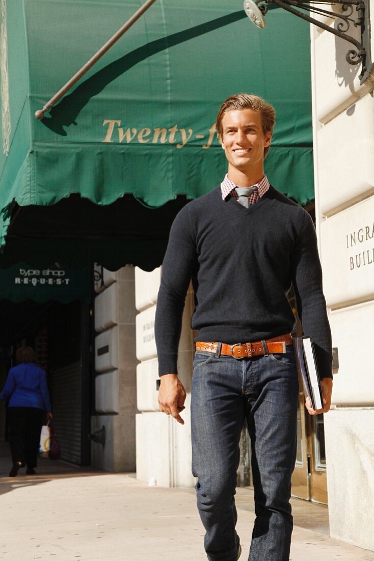 A young man wearing a jumper walking down the street holding the book