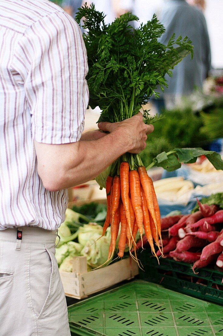 Mann mit einem Bund firscher Karotten auf dem Markt