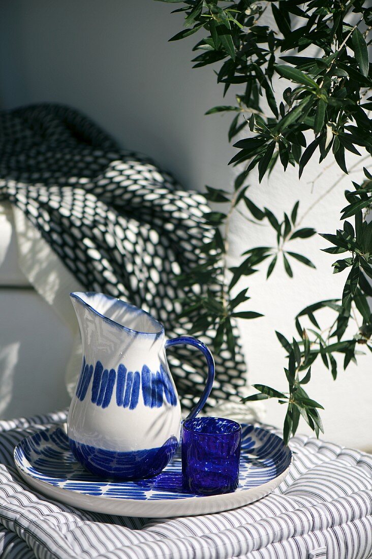 Blue and white painted jug with matching dish and blue glass on seat cushion