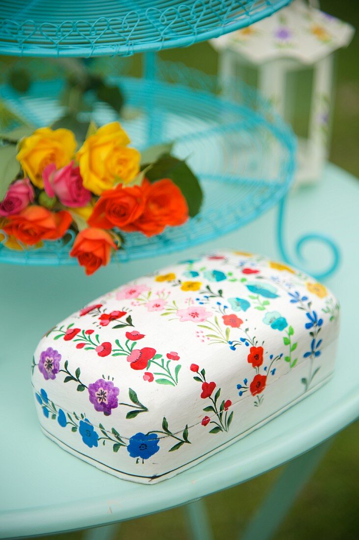 Tin with floral pattern and flowers on turquoise cake stand on garden table