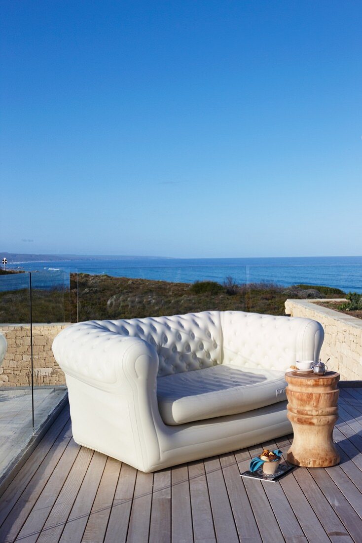 Elegant sofa and stool used as side table on wooden deck with sea view