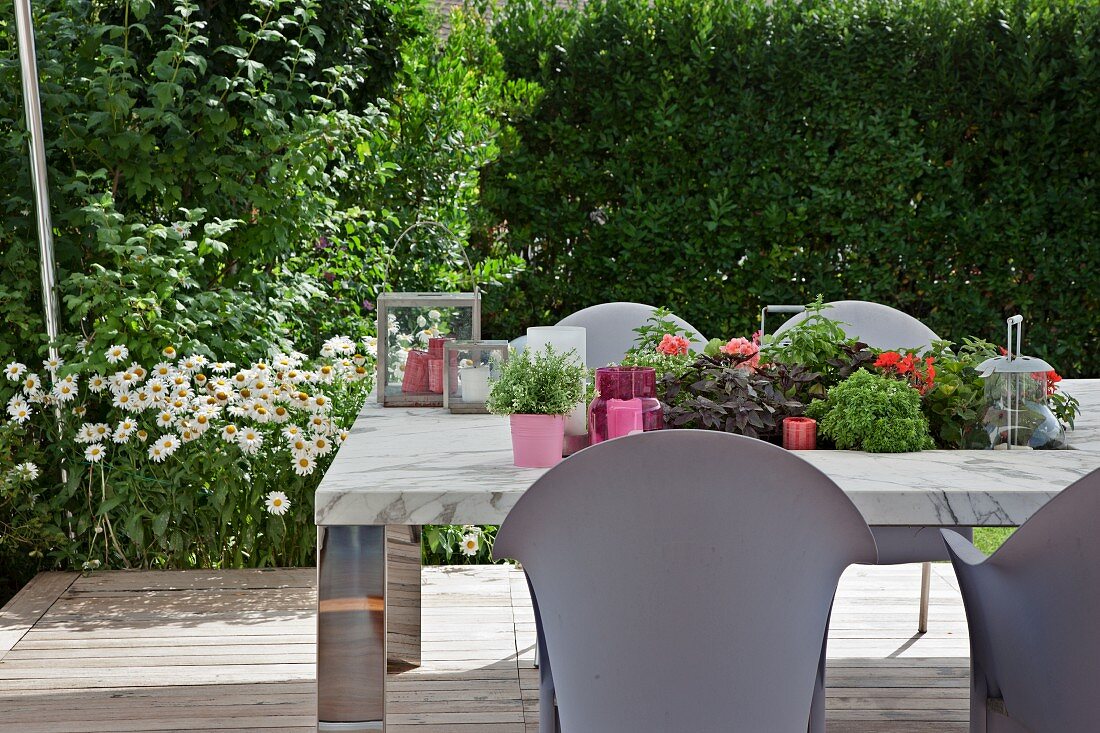 Pale grey outdoor chairs around table with recessed planting trough and ox-eye daisies flowering in garden in background
