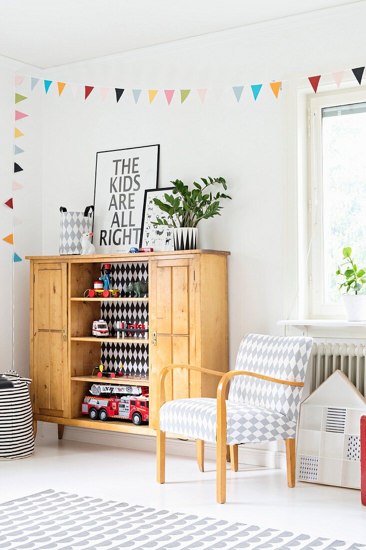 Armchair with diamond pattern and toys in rustic wooden cabinet below colourful bunting