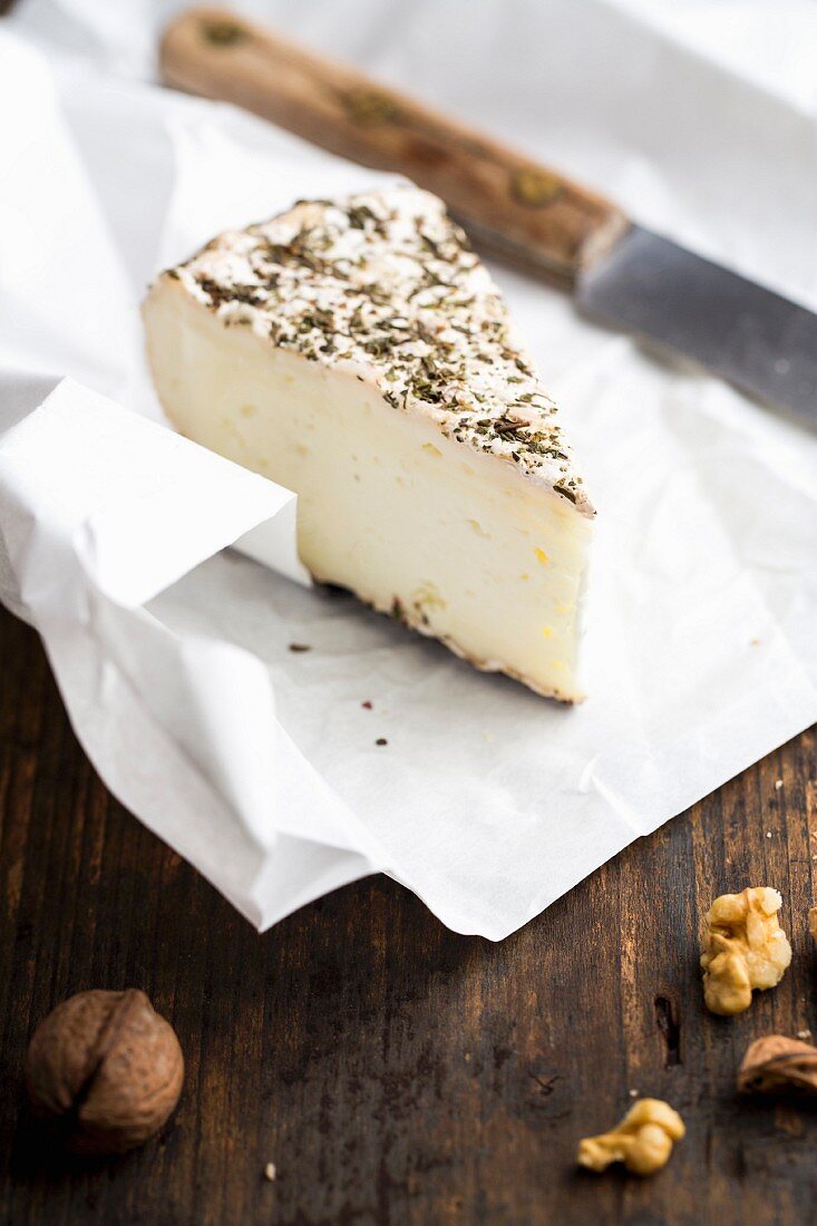 Goat's cheese with herbs on a piece of paper with a knife and walnuts