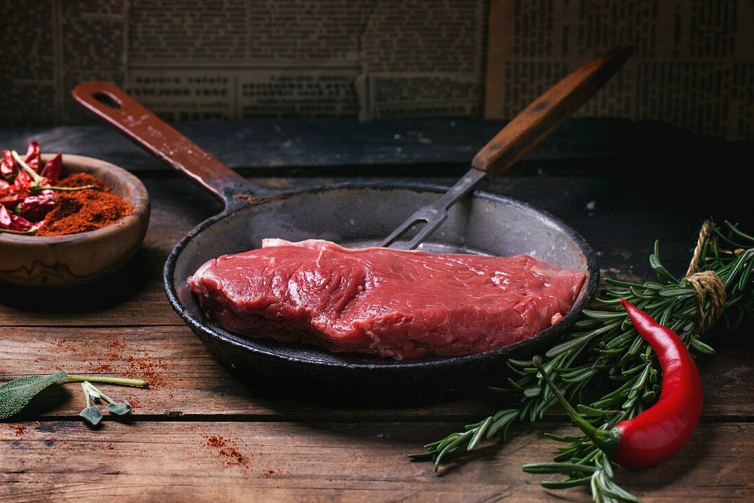 An arrangement featuring a raw beef steak, chillis and herbs