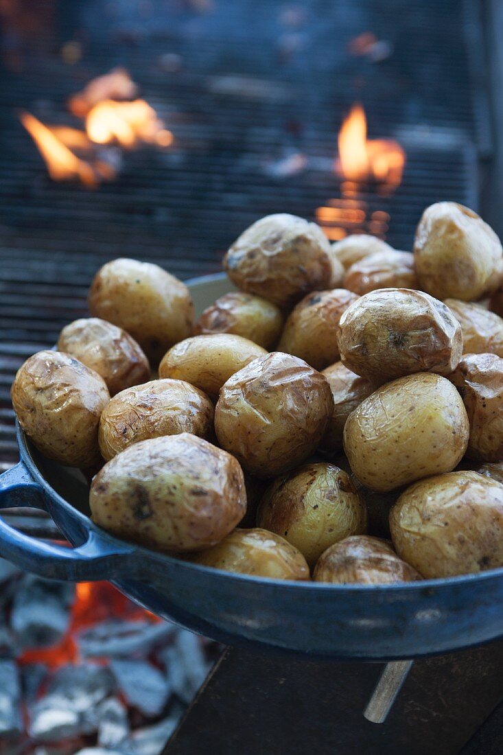 A pan of baked potatoes in front of a glowing grill