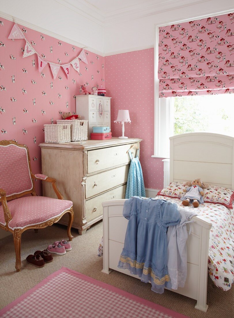 Girl's bedroom with pink patterned wallpaper and fabrics combined with white, country-house furnishings and antique armchair