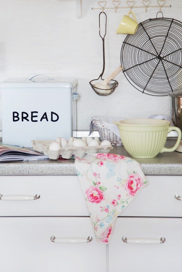 Kitchen utensils on worksurface below vintage ladle and cooling rack hung from hooks on wall