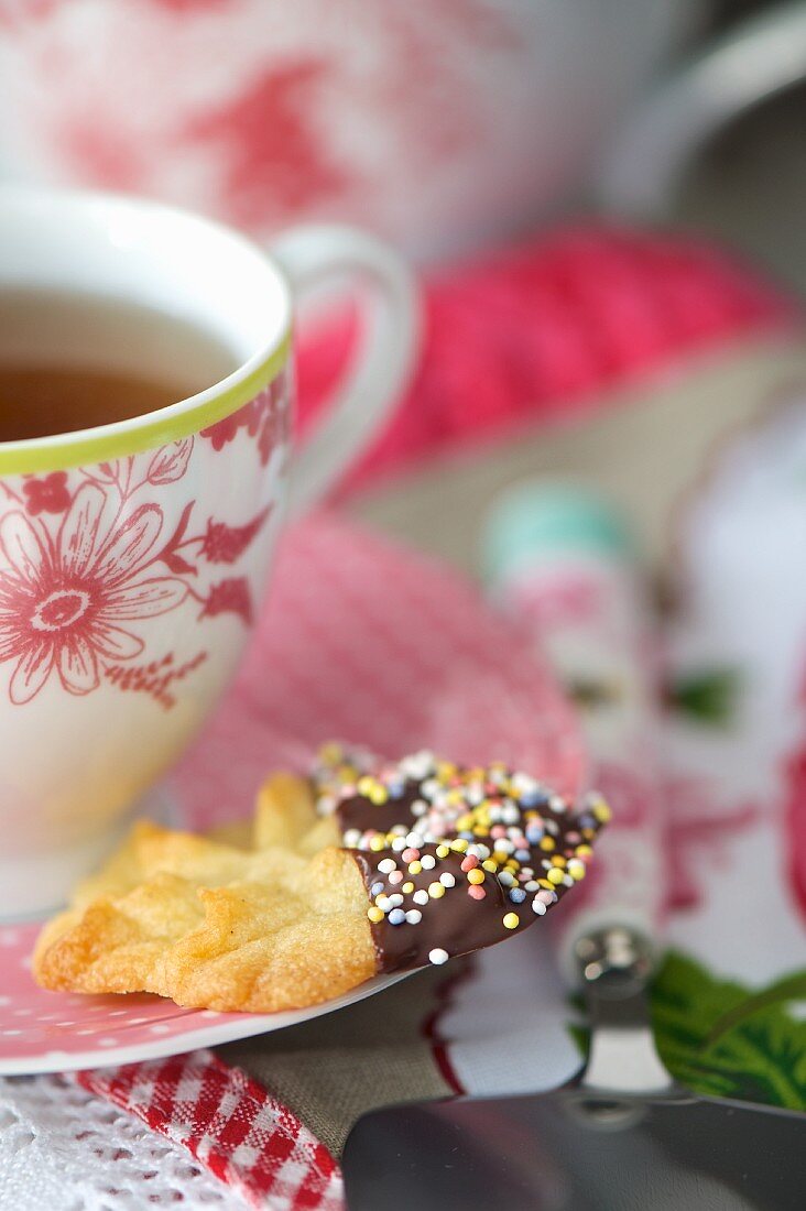 A chocolate biscuit decorated with sugar sprinkles served with a cup of tea