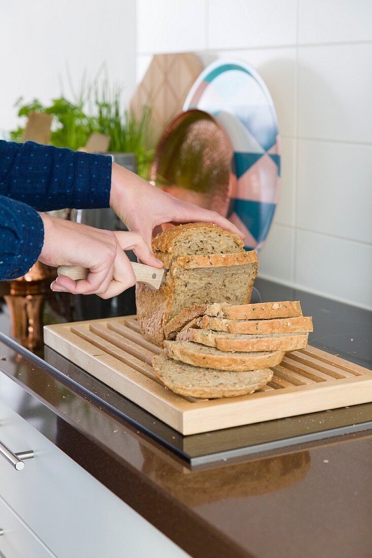 Hands slicing bread with knife in kitchen