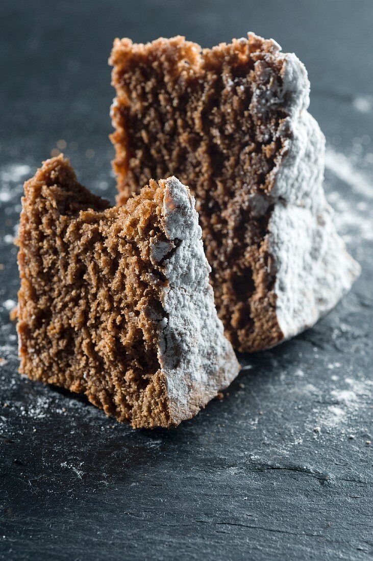 Two slices of chocolate cake with icing sugar, one with a bite taken out