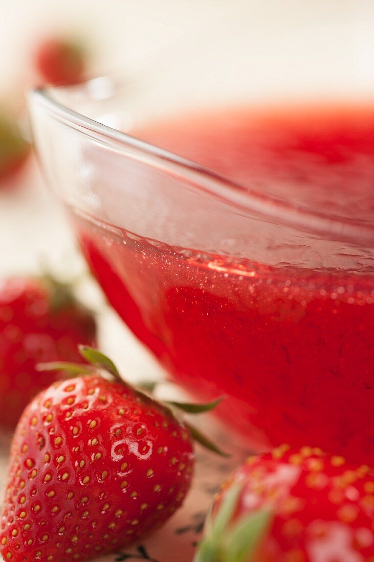 Erdbeermarmelade in Glasschale zwischen frischen Erdbeeren