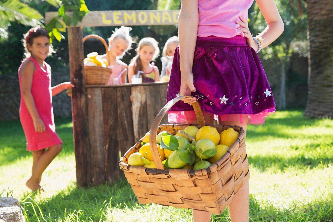 Mädchen trägt Korb mit Zitronen zu Limonadenstand