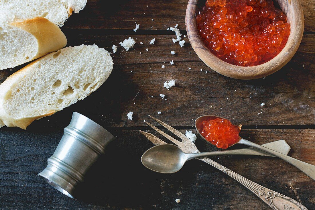 Red caviar in a wooden bowl with bread and old cutlery