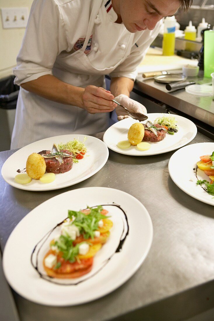 A young chef in a kitchen plating tuna tartare