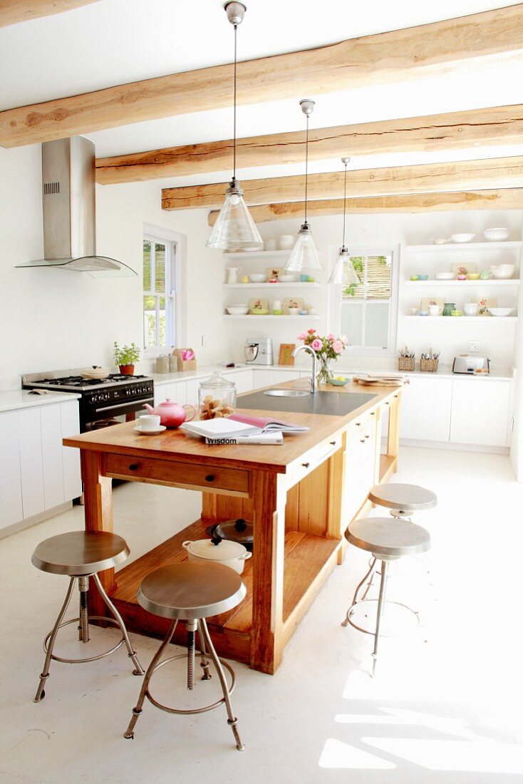 Vintage metal stools around free-standing, solid-wood island counter in bright, sunny kitchen with wood-beamed ceiling