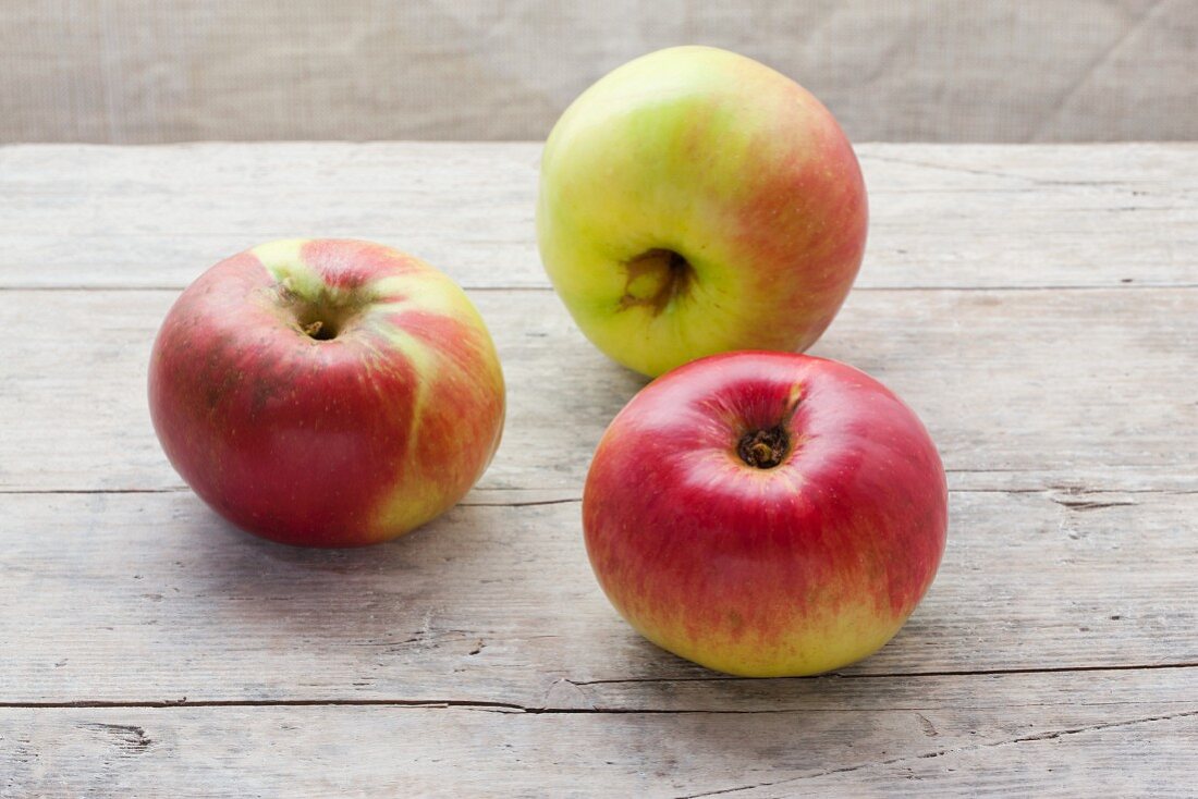 Drei Bio-Äpfel der Sorte Brettacher auf Holzuntergrund