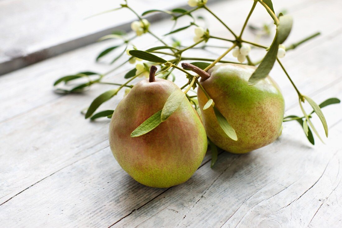 Two Vereinsdechant (Doyenne du Comice) pears and a sprig of mistletoe on a wooden surface