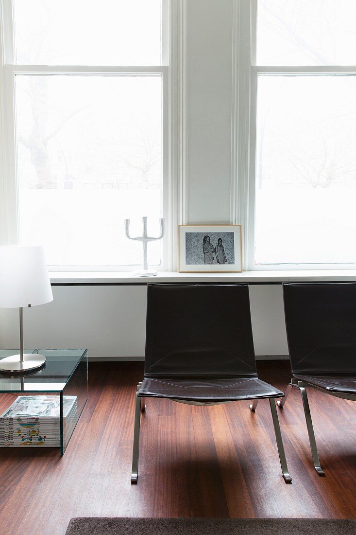 Metal and leather chairs next to table lamp on glass table in front of period-building windows