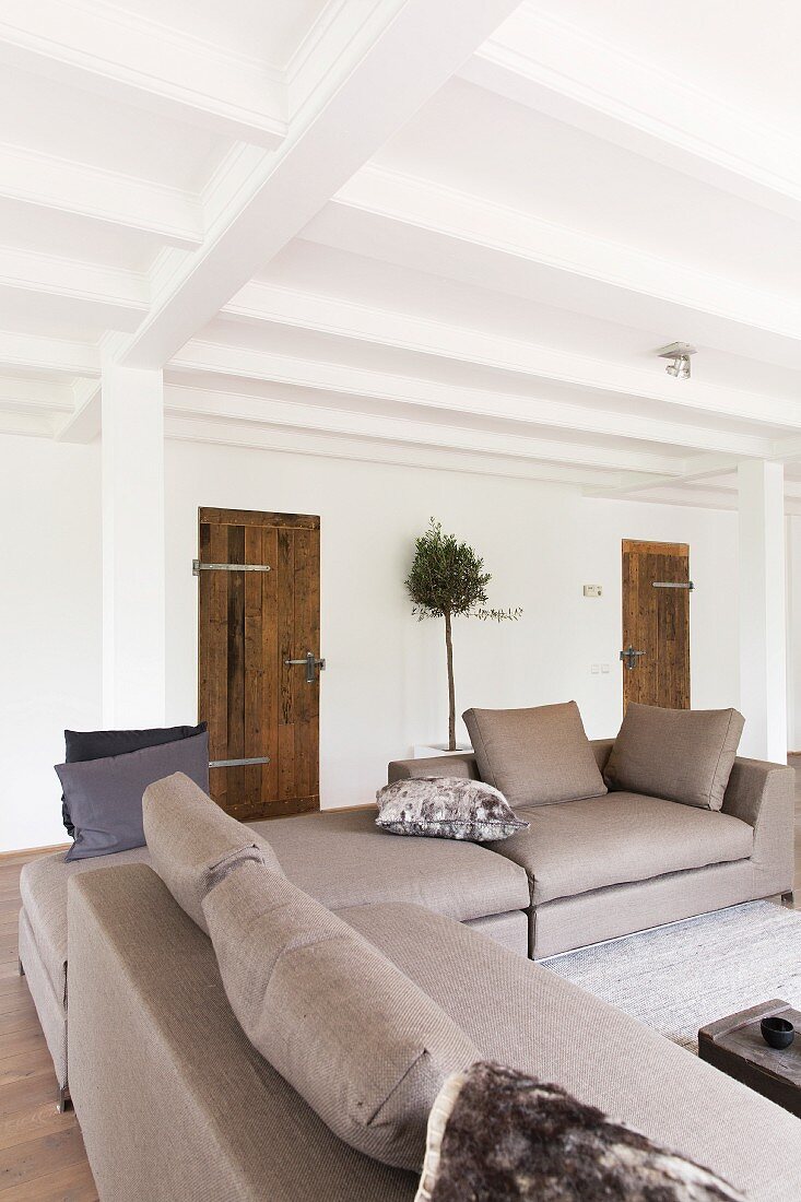 Elegant, pale grey sofa combination in open-plan interior with rustic charm and white, wood-beamed ceiling