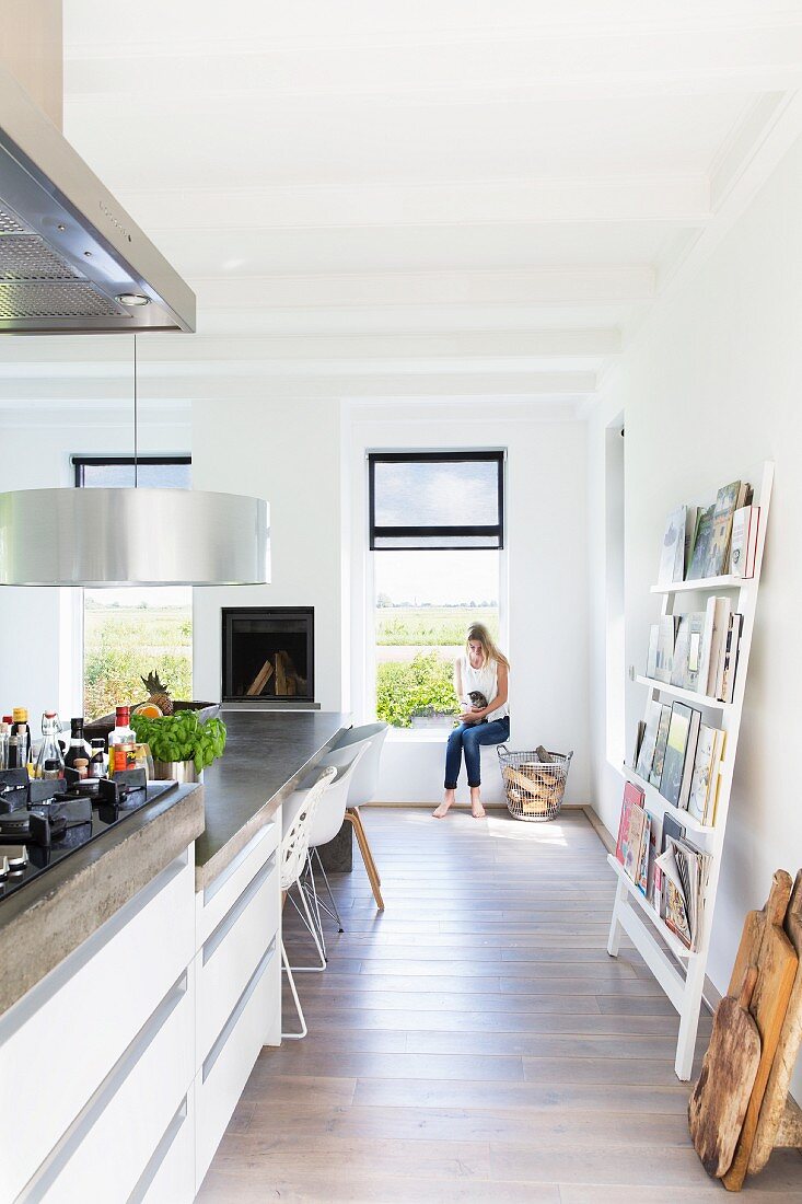 Designer kitchen counter continuing into dining table; young woman and cat sitting next to window in background