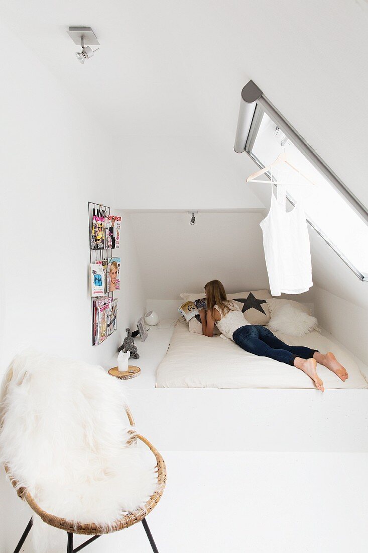 Modern teenager's bedroom with sloping ceiling and white sheepskin blanket on wicker chair